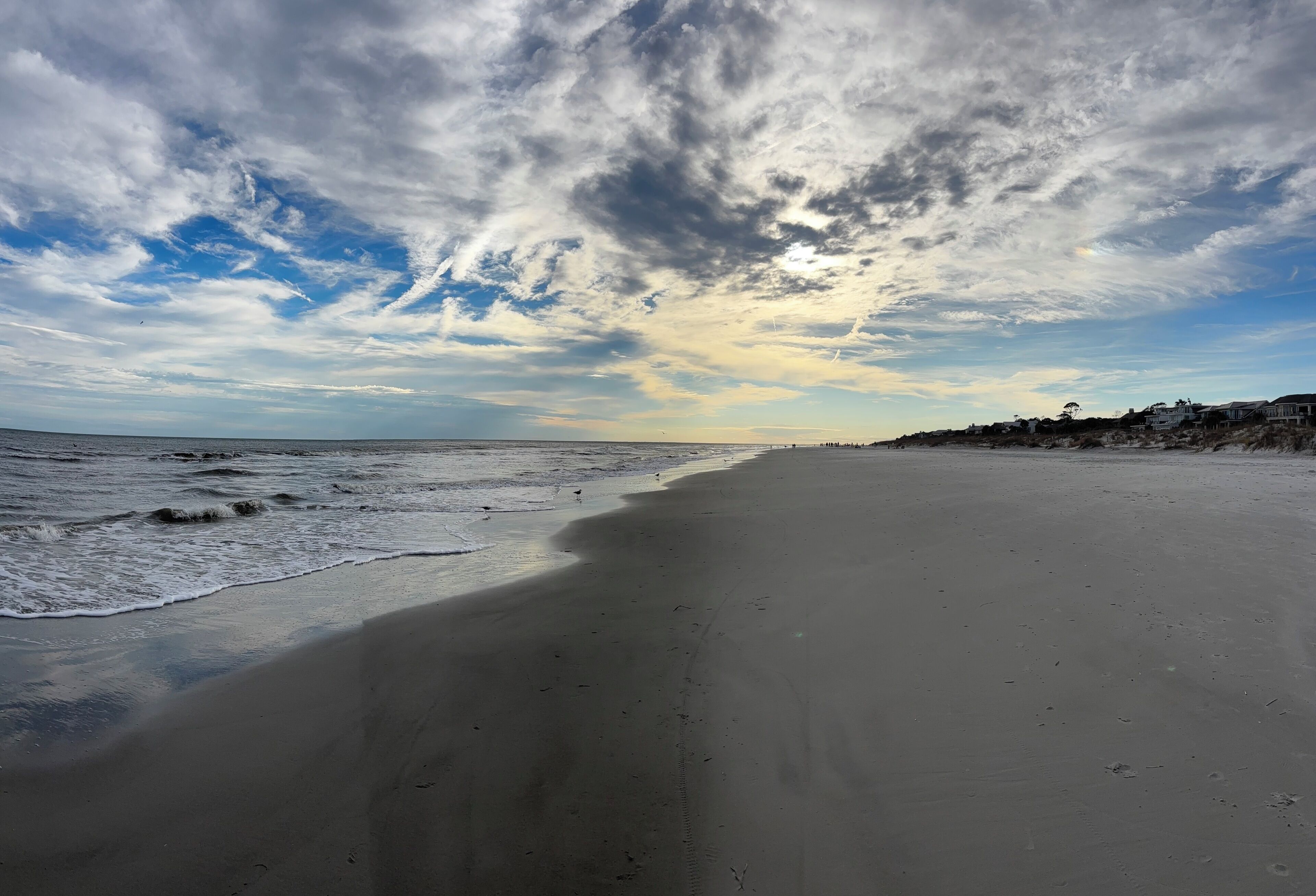 Een strand met een brede zandkust, een rustige zee en een gedeeltelijk bewolkte lucht.