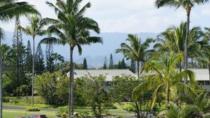 A tropical resort with palm trees, a road, and a mountain range in the background. - Cozy 2BR Condo Great for Families (Princeville)