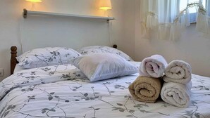 Un llit ben fet amb roba de llit de motius florals, dues làmpades penjades a la paret i una finestra amb cortines translúcides.