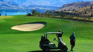 En golfbana med en sandbunker, en golfbil och en person som står i närheten.