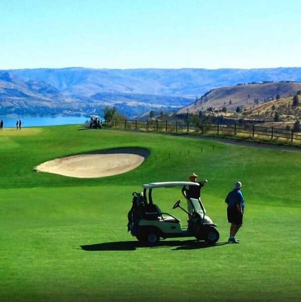 A golf course with a sand bunker, a golf cart, and a person standing nearby. - Waterfront, Stunning Views, Private Beach, and Close To Concerts (Quincy)