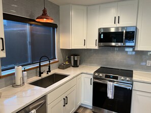 A modern kitchen with white cabinets, a stainless steel stove, a microwave, and a sink with a window above it. - Waterfront, Stunning Views, Private Beach, and Close To Concerts (Quincy)