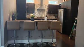 Een moderne keuken met een centraal eiland, barstoelen, roestvrijstalen apparatuur en een accentmuur van baksteen.