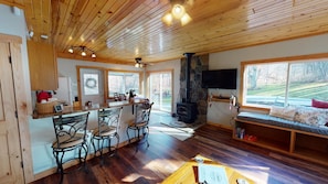 Een gezellig cabin interieur met een stenen open haard, houten plafond en een groot raam met uitzicht op de natuur.