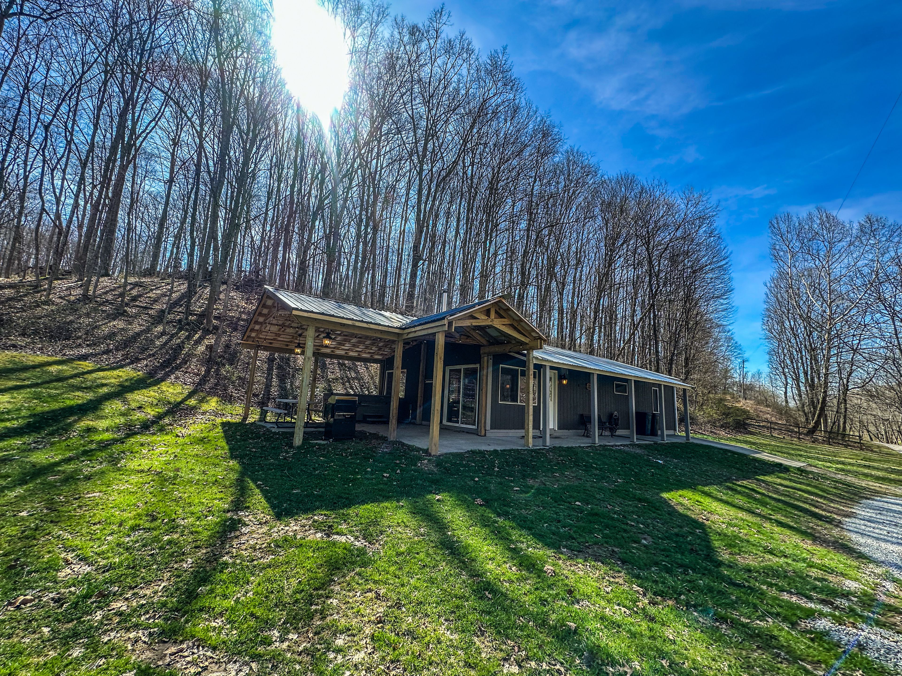 A covered outdoor area with a wooden structure, surrounded by trees and a clear sky.