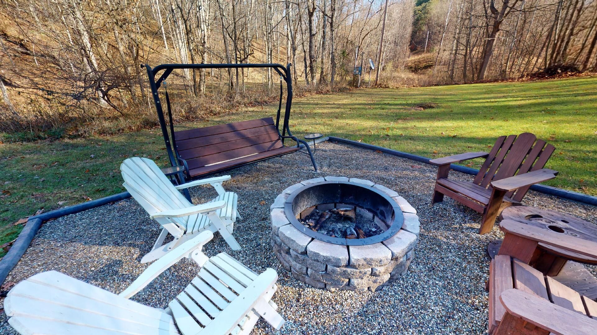 An outdoor seating area with Adirondack chairs, a swing, and a fire pit.