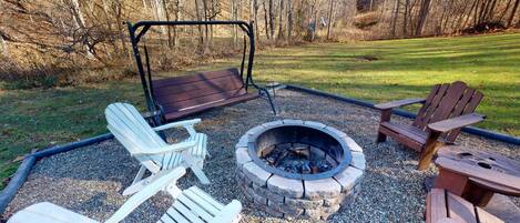 An outdoor seating area with Adirondack chairs, a swing, and a fire pit.