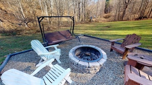 Een gebied met een vuurkorf, Adirondack stoelen en een schommelset.