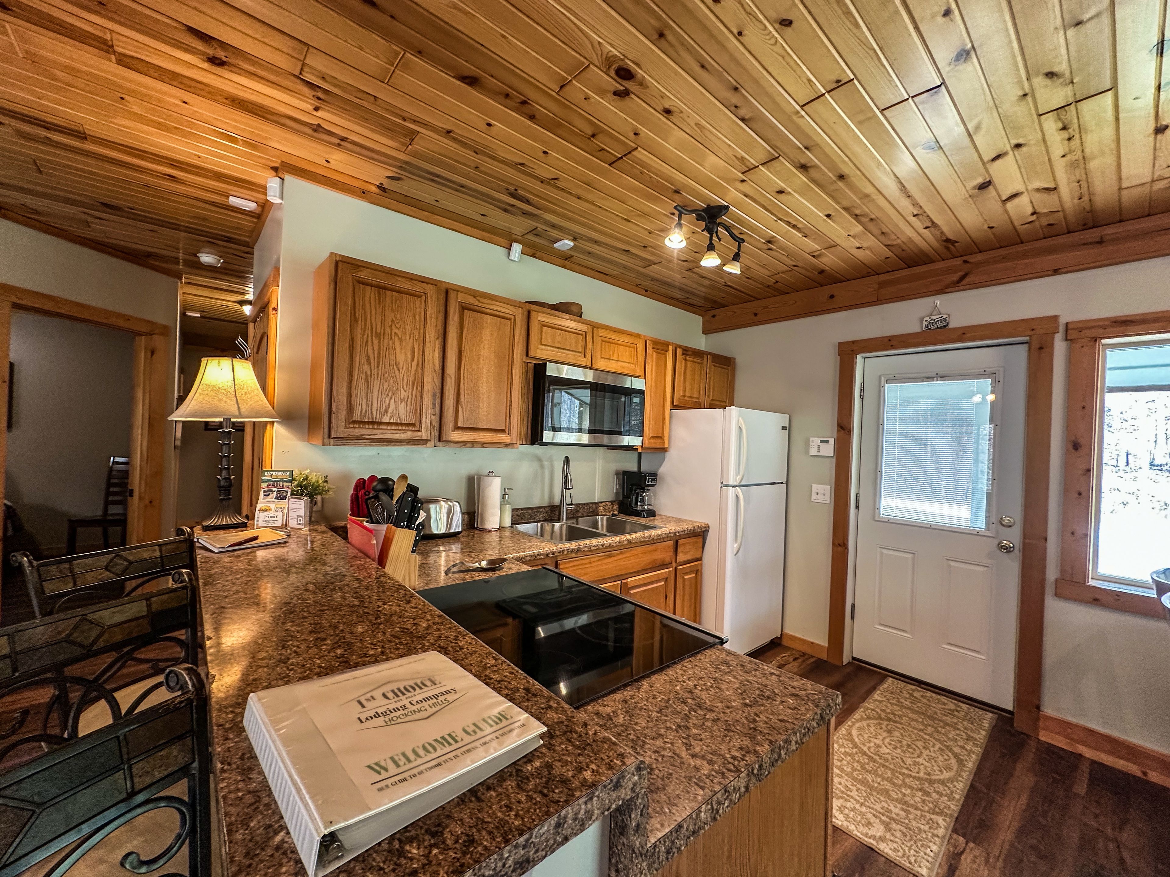 A kitchen with wooden cabinets, a microwave, a refrigerator, a sink, and a welcome guide on the counter.