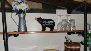 A kitchen shelf with a metal bear figurine, a vase with flowers, and glassware. - Kokomo Farms - Cozy Cottage on the Farm (Live Oak)