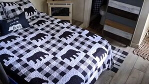 A bedroom with a checkered bedspread featuring bear patterns, a bedside table with a lamp, and a view of a wooden deck. - Kokomo Farms - Cozy Cottage on the Farm (Live Oak)