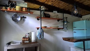 A kitchen with wooden shelves, a vintage refrigerator, and hanging utensils. - Kokomo Farms - Cozy Cottage on the Farm (Live Oak)