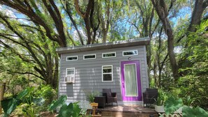 A small cabin with a purple door, surrounded by trees and a wooden deck. - Kokomo Farms - Cozy Cottage on the Farm (Live Oak)
