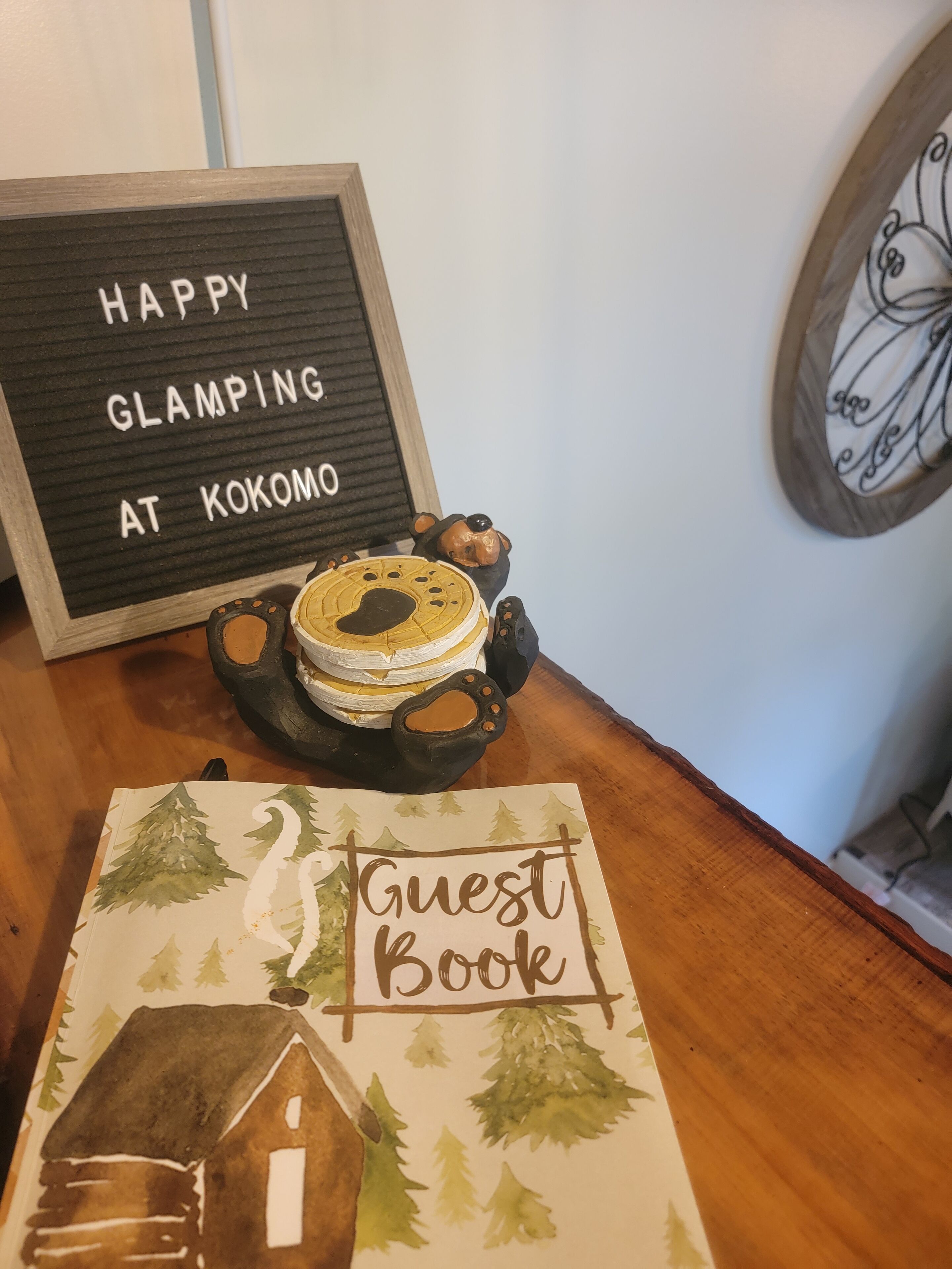 A wooden table with a sign that reads "HAPPY GLAMPING AT KOKOMO" and a small bear figurine.