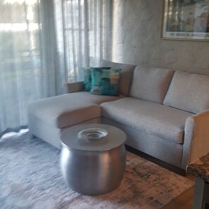 A living room with a beige sofa, a round metallic side table, and a painting on the wall.