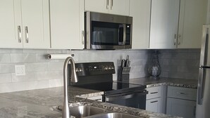 Una cocina con gabinetes blancos, un lavamanos de acero inoxidable, un microondas y una estufa.