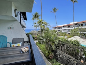 A balcony with a table, chairs, and a bowl of seashells. There are palm trees and a view of the ocean.