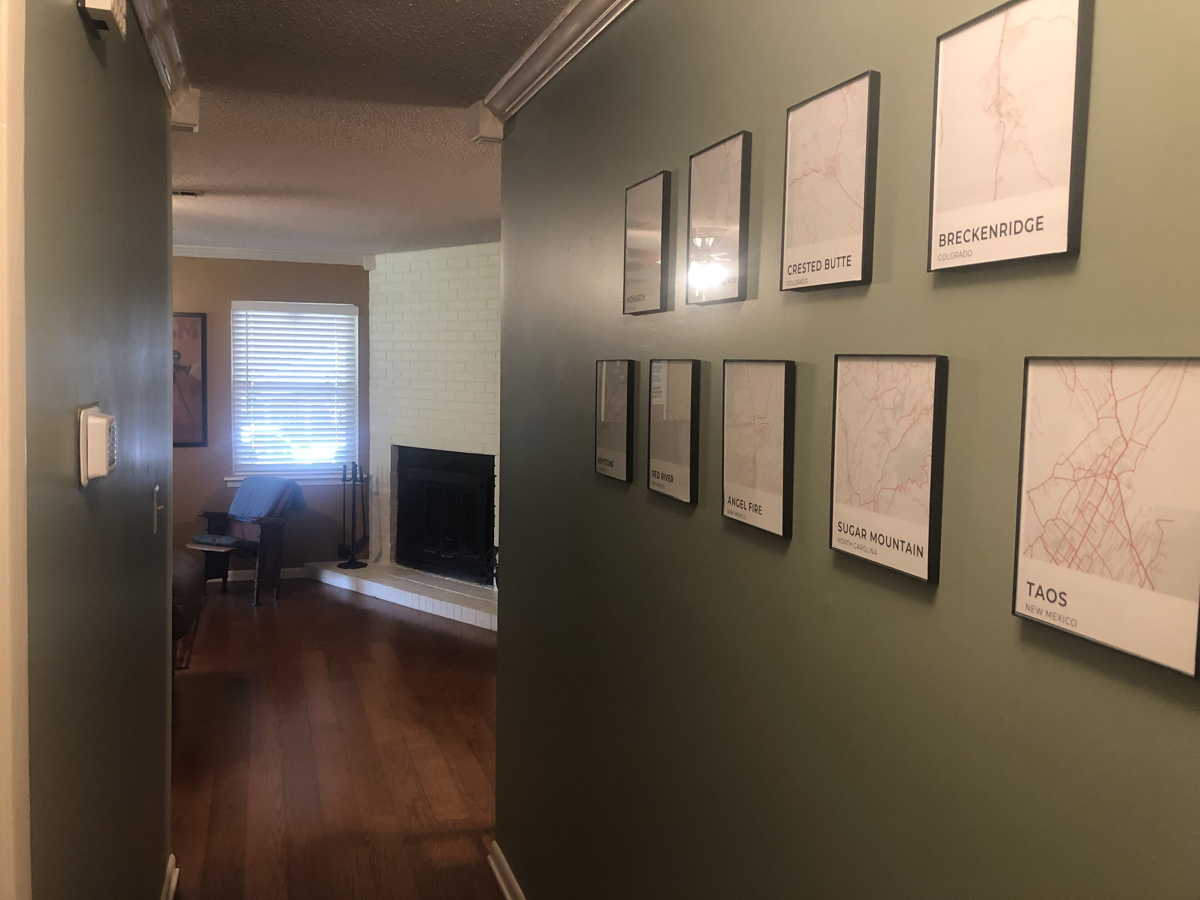 Un pasillo con mapas enmarcados en la pared, una chimenea y una puerta que da a otra habitación.