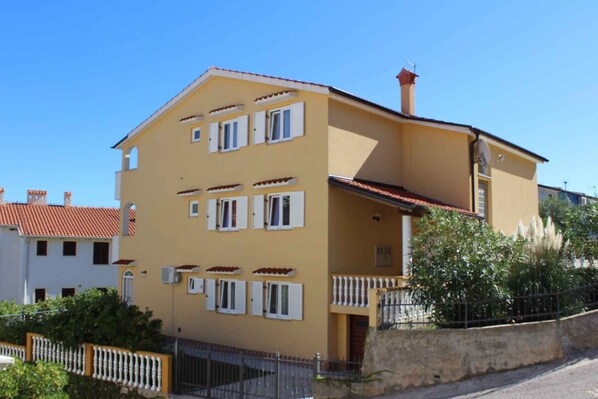 A two-story building with a yellow facade, white window shutters, and a red-tiled roof.