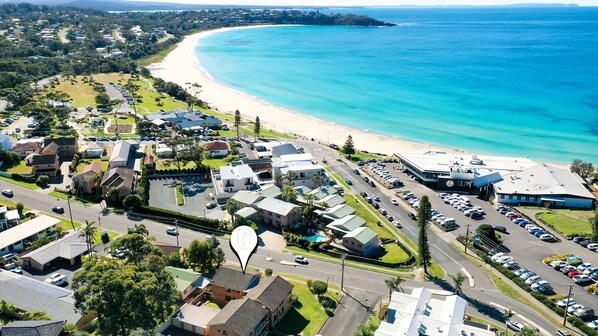An aerial view of a coastal residential area with a beach, houses, and a parking lot.