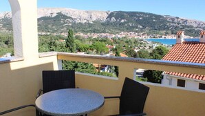 A balcony with a round table and chairs, overlooking a town with buildings and a mountain in the background.