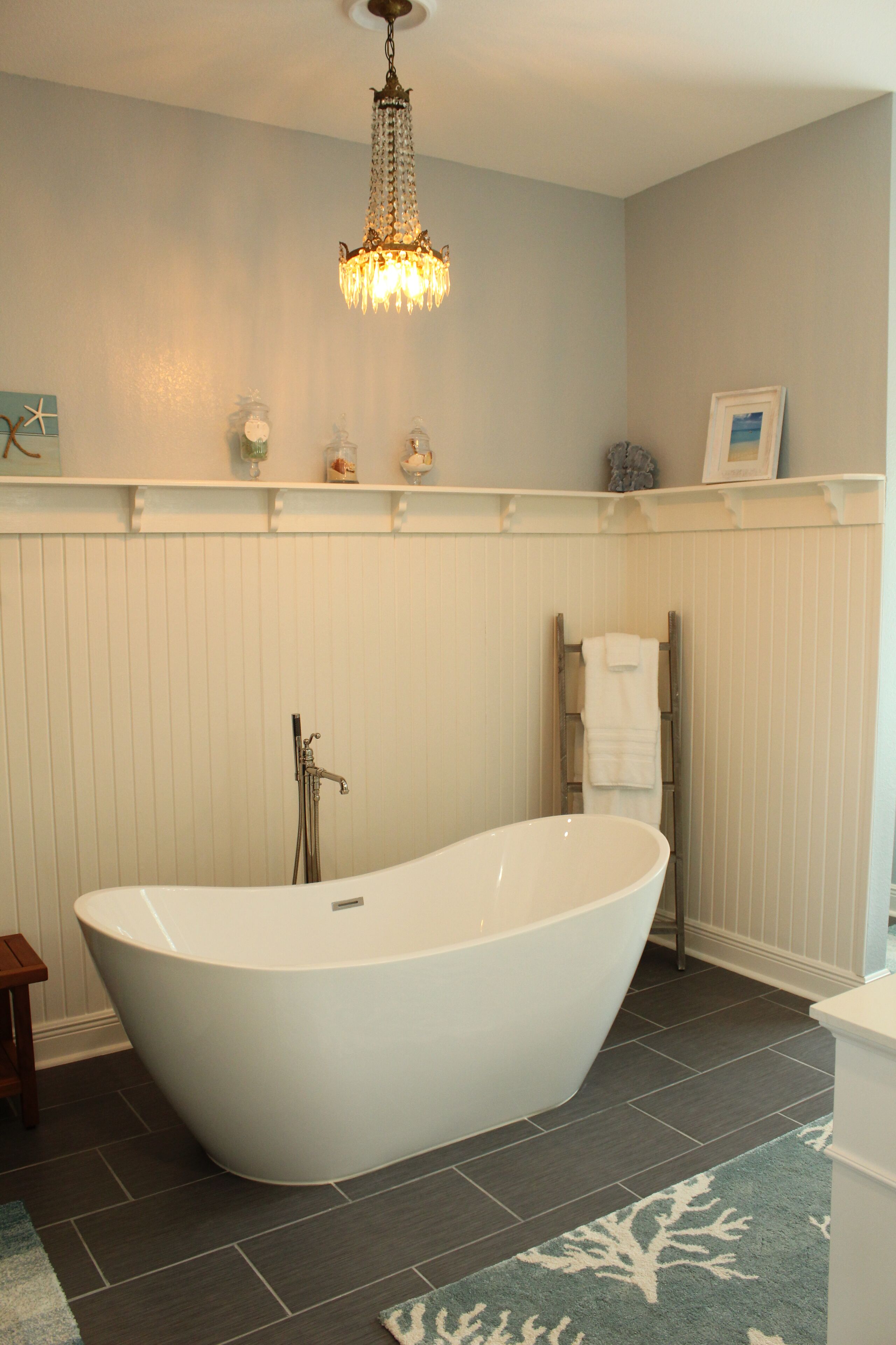 A bathroom with a freestanding bathtub, a chandelier, and a towel rack.