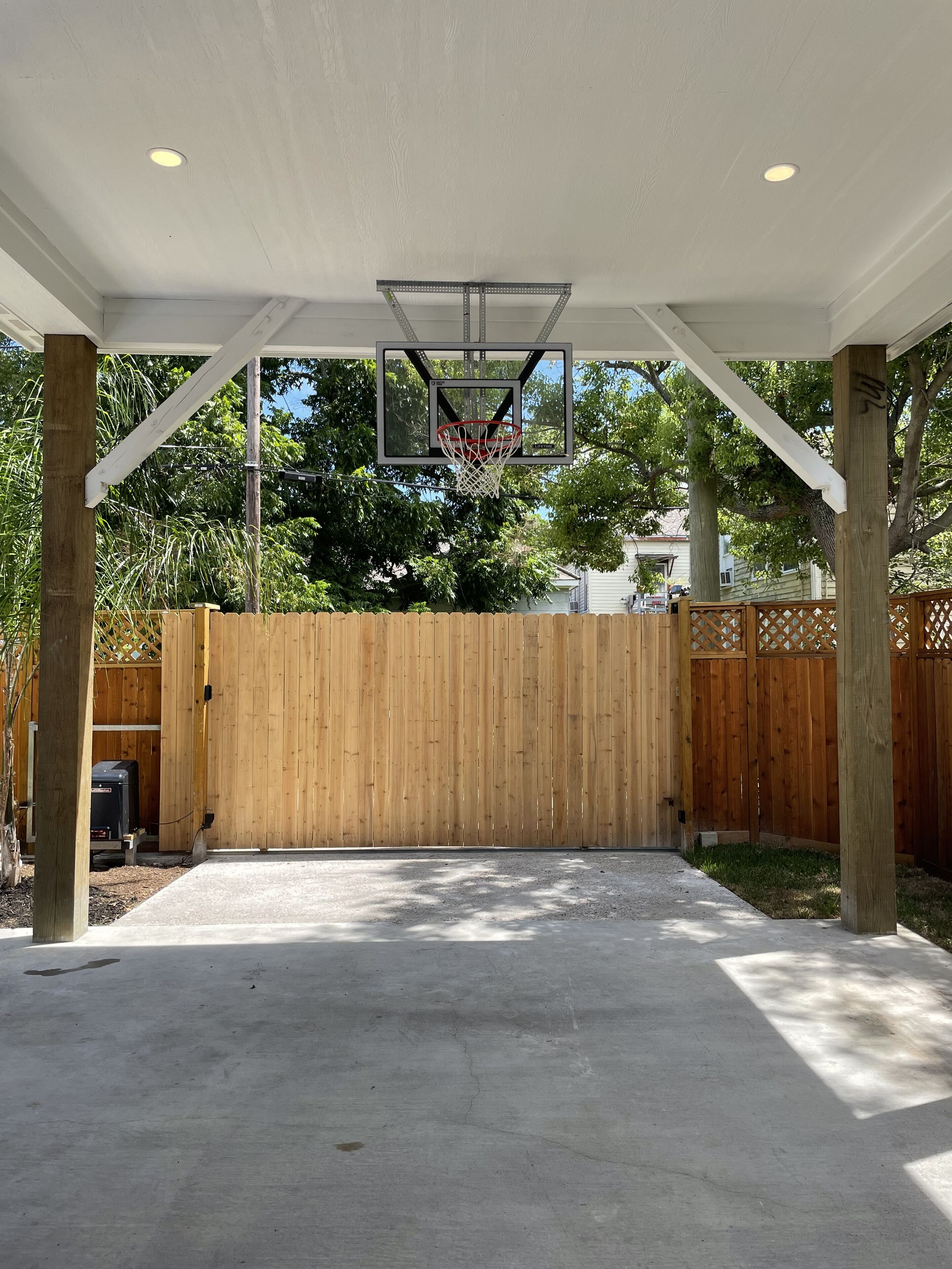 Ein Basketballplatz im Freien mit Holzzaun, Betonboden und einem Basketballkorb.