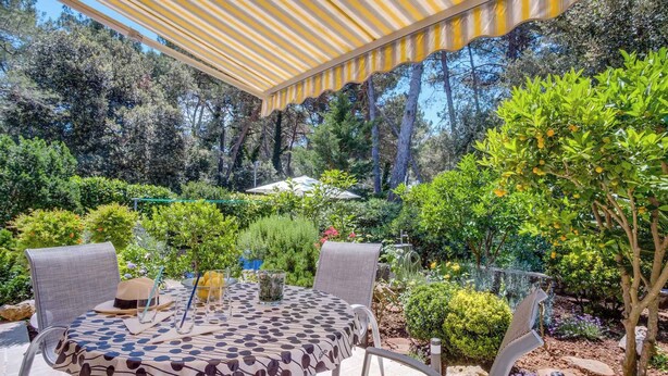 An outdoor patio with a round table and chairs, surrounded by lush greenery and trees.