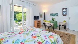 A bedroom with a bed, a TV, a table with chairs, and a view of the outdoors.