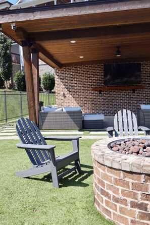 An outdoor patio with Adirondack chairs, a fire pit, and a brick wall.