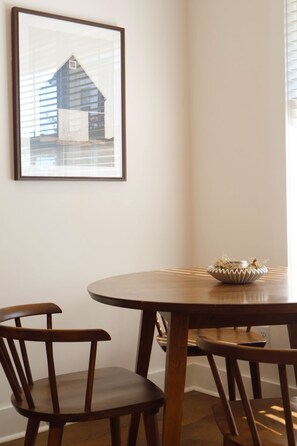 A dining area with a round wooden table, two chairs, and a framed picture on the wall.