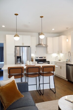 A modern kitchen with white cabinetry, stainless steel appliances, and pendant lighting.