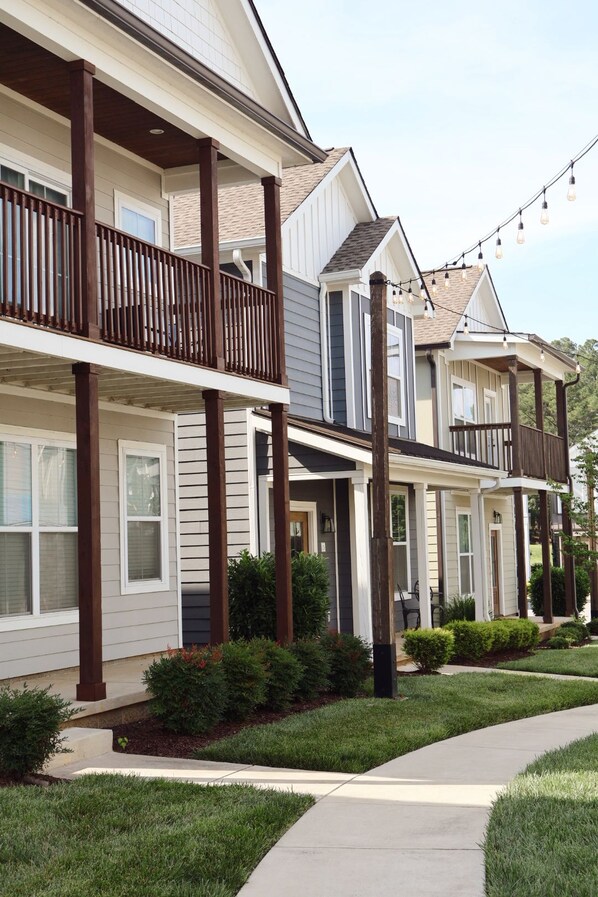 A row of townhouses with balconies, a sidewalk, and string lights.