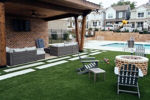 Un giardino con un muro in mattoni, un pergolato di legno, una piscina e mobili da esterno.