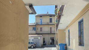 Una calle estrecha flanqueada por edificios, un coche aparcado y un contenedor azul.