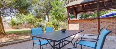 Un patio al aire libre con un muro de ladrillo, una pérgola de madera y una mesa con sillas azules.