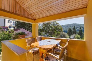 Un espacio de estar al aire libre cubierto, con una mesa y sillas, techo de madera y vistas a zonas verdes y colinas.