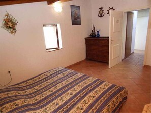 Een slaapkamer met een bed, een dressoir, een klein raam en een deur naar een andere kamer.