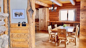 Un intérieur rustique en bois, avec un coin repas, des éléments en pierre et un lustre.