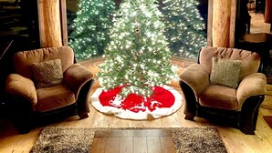 Une pièce chaleureuse avec deux fauteuils en cuir, un plancher en bois et une grande fenêtre donnant sur deux sapins de Noël décorés.