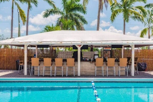 Un espace extérieur aménagé, abrité et doté de chaises, avec une piscine en premier plan.