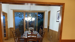 A dining area with a long wooden table and chairs, a chandelier, and a view through large glass doors. - Views, hot tub, spacious 3Bd, 3Ba w Tesla Charger (Robbinsville)