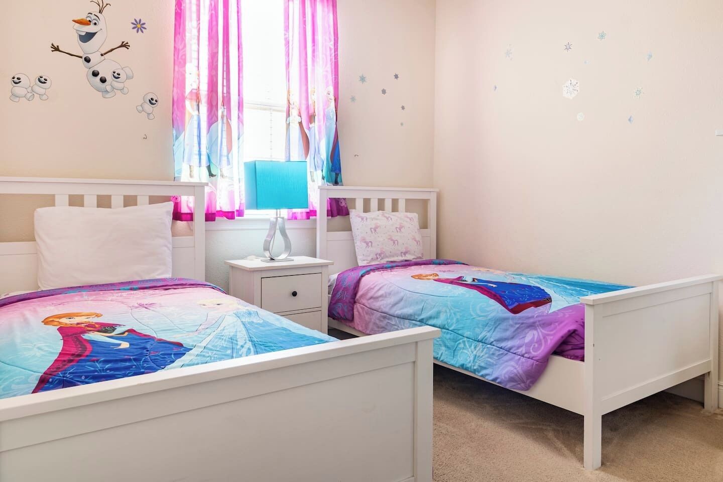 A bedroom with two beds, a nightstand, a lamp, and a window with curtains.
