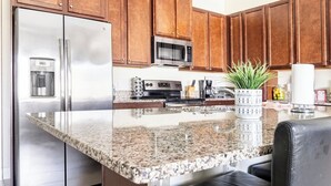 A kitchen with granite countertops, stainless steel appliances, wooden cabinets, and a black leather chair. - Luxury Villa, Clubhouse, Pool, 15 mins from Disney (Davenport)