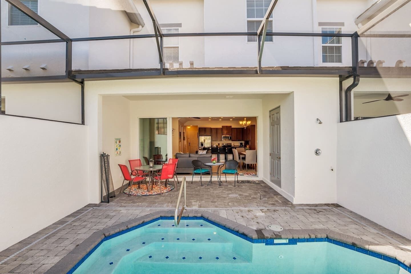 Ein Wohnhaus mit Schwimmbad, einem Essbereich mit roten Stühlen und einer durchgehenden Tür einsehbarer Küche.