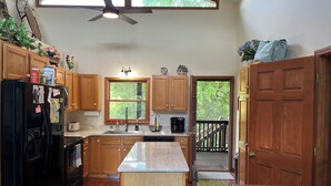 A kitchen with wooden cabinets, a black refrigerator, a window with a view of greenery, and a ceiling fan. - 2 Views!  Front view of Lake Glenville & back view of Christmas Tree farm! (Glenville)