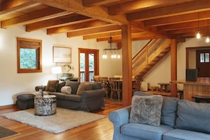 A spacious living room with wooden beams, a staircase, and a dining area. - Clayoquot Surf Retreat (Tofino)