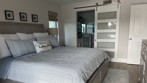 A bedroom with a bed, a wardrobe, and a bathroom visible through an open door. - Gated FoxFire Naples First-Floor/End-unit Amazing Water/Course View 27-Hole Golf (Naples)