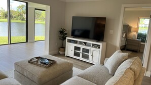 A spacious living room with a large flat-screen TV, a white entertainment unit, and a beige sofa. - Gated FoxFire Naples First-Floor/End-unit Amazing Water/Course View 27-Hole Golf (Naples)