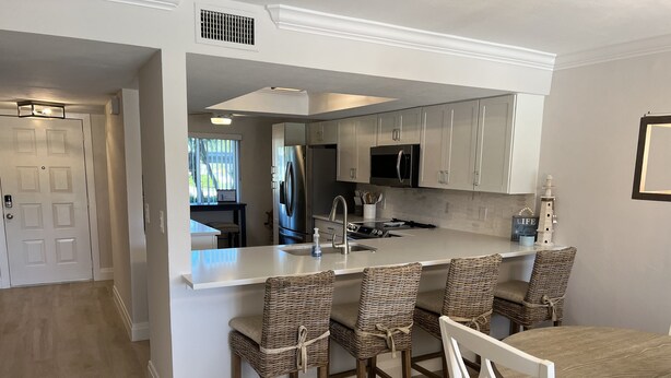 A modern kitchen with a central island, bar stools, and a dining table. - Gated FoxFire Naples First-Floor/End-unit Amazing Water/Course View 27-Hole Golf (Naples)